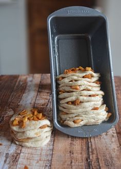 a pan filled with food sitting on top of a wooden table next to a loaf of bread