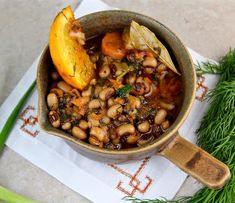 a bowl filled with beans and carrots on top of a napkin next to some herbs