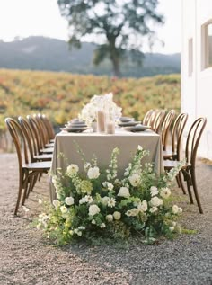 the table is set with white flowers and candles for an elegant dinner in the vineyard