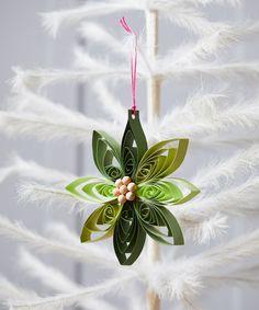 a green ornament hanging from a white christmas tree with feathers on the branches