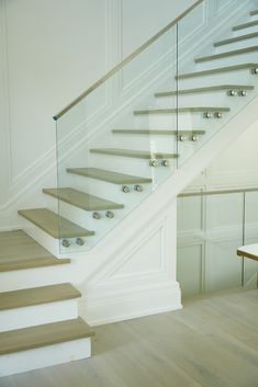 a white staircase with glass railing and wooden steps