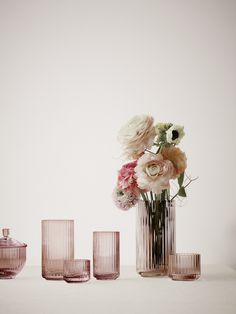 vases and glasses on a table with flowers in the middle one is pink, while the other two are clear