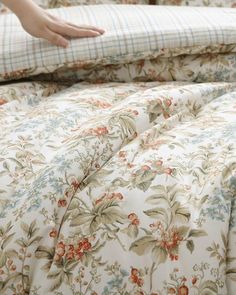 a person reaching for something on top of a bed with floral sheets and pillow cases