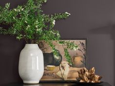 a white vase sitting on top of a table next to a painting and some plants