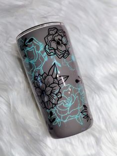 the tumbler is decorated with blue and black flowers on it's side, sitting on a white furnishing