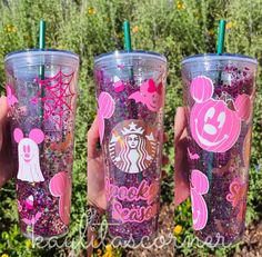 three starbucks tumblers with minnie mouse and mickey mouse ears on them, one is pink and the other has purple sprinkles