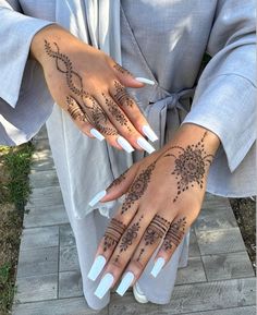 a woman's hands with henna tattoos on her left hand and white fingernails