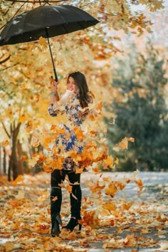 a woman is holding an umbrella in the leaves