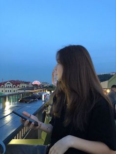 a woman looking at her cell phone while standing on a balcony overlooking the city skyline