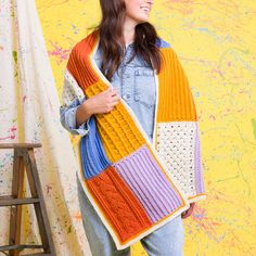 a woman standing in front of a wall wearing a multicolored knitted scarf