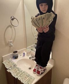 a little boy standing on a bathroom sink holding money