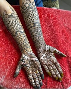 two hands with henna tattoos on them sitting next to each other in front of a red blanket