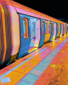 a colorful train stopped at a station with its doors open and lights on the side