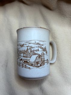 a coffee cup with a farm scene drawn on the outside and inside is sitting on a blanket