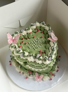 a green birthday cake decorated with butterflies and flowers on a white plate in a box