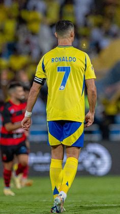 a soccer player in yellow and blue uniform walking on the field with his foot up