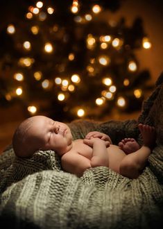 a baby laying on top of a blanket next to a christmas tree with lights in the background