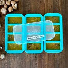 three plastic trays filled with soup next to mushrooms on a wooden table, one is empty and the other two are open