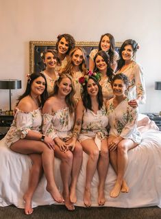 a group of women sitting on top of a bed in matching robes and flower crowns