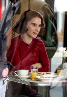 a woman sitting at a table with a cup of coffee and orange juice in front of her