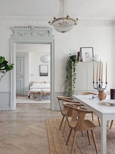 a dining room with white walls and wooden chairs, a chandelier hanging from the ceiling