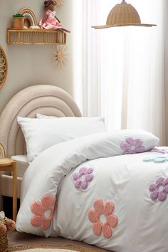 a white bed with pink flowers on the comforter and pillow cases in front of a window