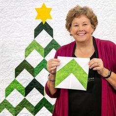 a woman holding up a piece of paper in front of a quilted christmas tree