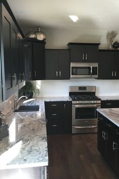 a kitchen with stainless steel appliances and black cabinets, marble counter tops, and wood flooring