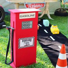 a red gas pump sitting on top of a lush green field next to traffic cones