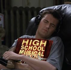 a man sleeping with headphones on his ears while holding a high school musical book