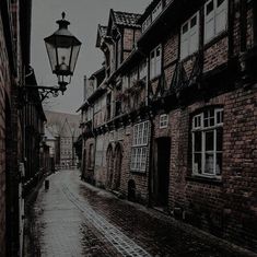 an old fashioned street light in the middle of a cobblestone road with brick buildings on both sides