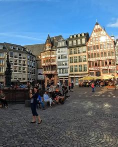 people are sitting on benches in the middle of a cobblestone square with buildings