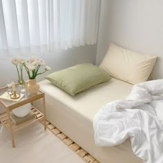 a bed with white sheets and pillows in a room next to a table with flowers on it