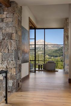 a large stone fireplace in the middle of a room with wood flooring and windows