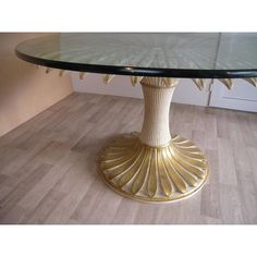 a round glass table with gold decoration on it's base and wood flooring