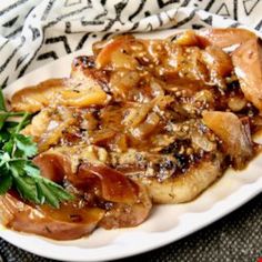 a white plate topped with meat covered in sauce and onions on top of a black and white table cloth