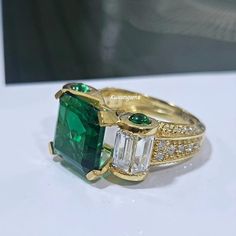 an emerald and diamond ring is displayed on a table