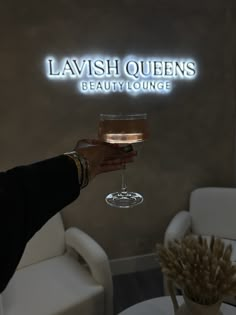 a woman holding a wine glass in front of a sign that says lavish queens beauty lounge