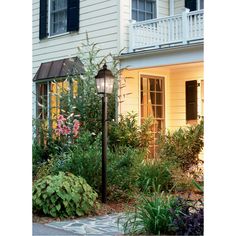 a lamp post in front of a house with flowers and plants around it, next to a walkway