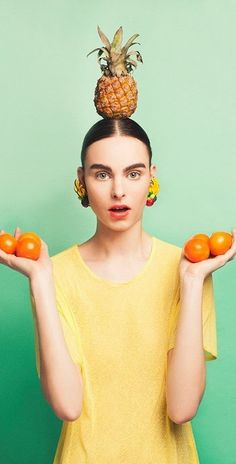 a woman holding two oranges in her hands and a pineapple on top of her head