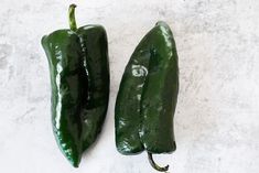 two green peppers sitting next to each other on a white counter top, with one pepper still in it's pod