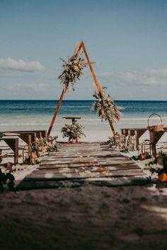 an outdoor ceremony set up on the beach with flowers and greenery at the end