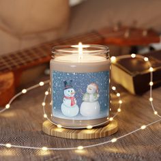 a candle that is sitting on a table with some string lights and a guitar in the background