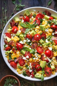 a bowl filled with corn, tomatoes and avocado on top of a wooden table