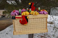 a wooden box filled with plastic birds on top of a snow covered ground next to trees