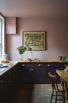 a kitchen with purple painted walls and wooden furniture, along with a painting on the wall