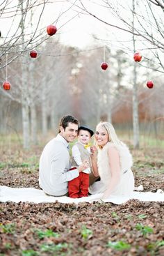 a man, woman and child are sitting on the ground in an apple orchard with apples hanging above them