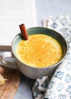 a cup filled with orange juice next to an open book and cinnamon on the table