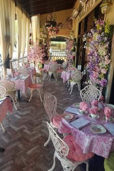 an outdoor dining area with tables and chairs covered in pink tablecloths, flowers on the wall