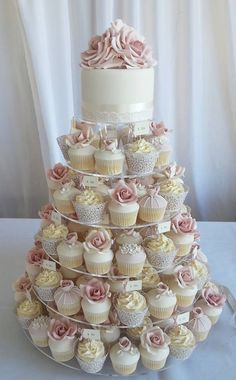 a three tiered wedding cake with cupcakes on the bottom and pink roses on top